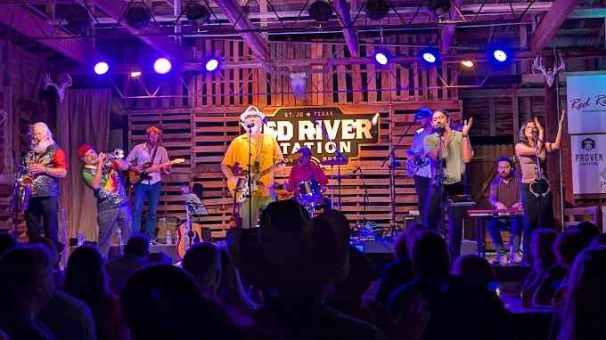Large horn-section band playing under purple lights inside the Red River Station barn