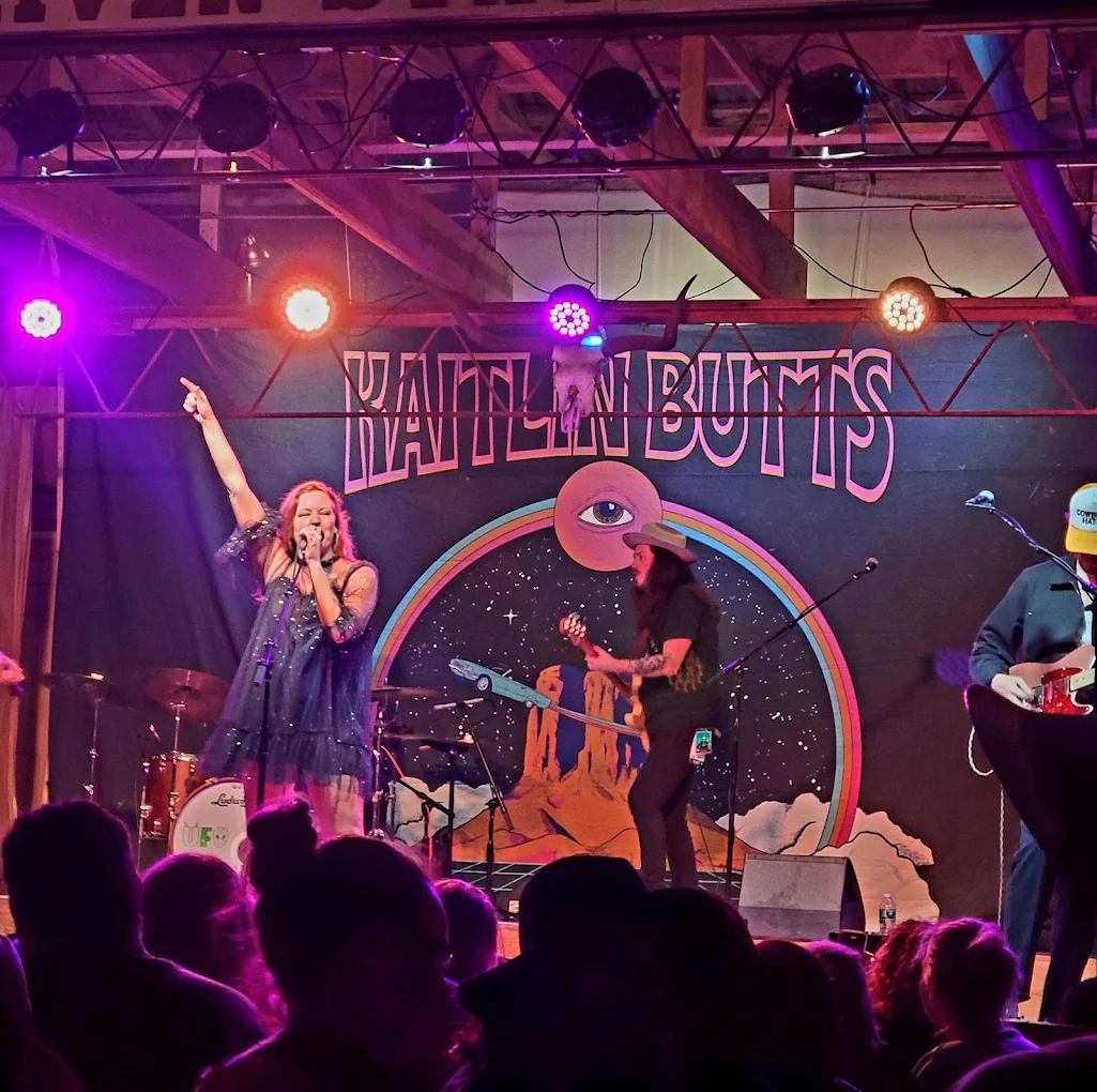 Kaitlin Butts singing to a packed crowd under pink and purple stage lights at Red River Station