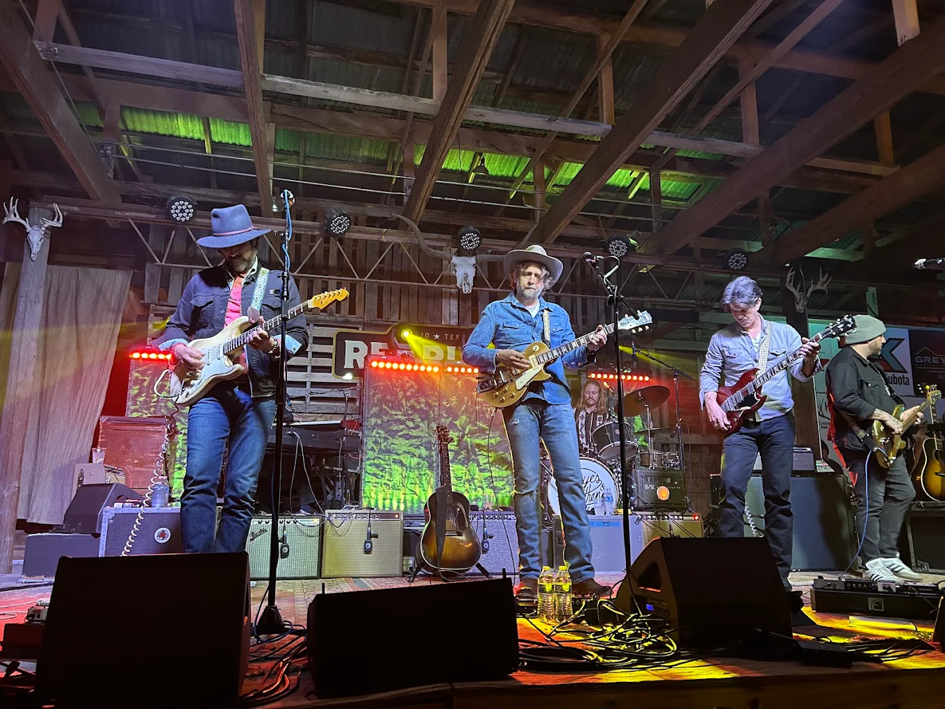 Four guitarists and a drummer on stage under warm amber lighting