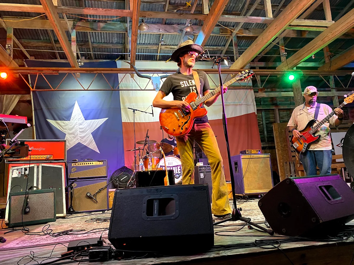 Guitarist in a straw hat and bassist performing in front of the Texas flag