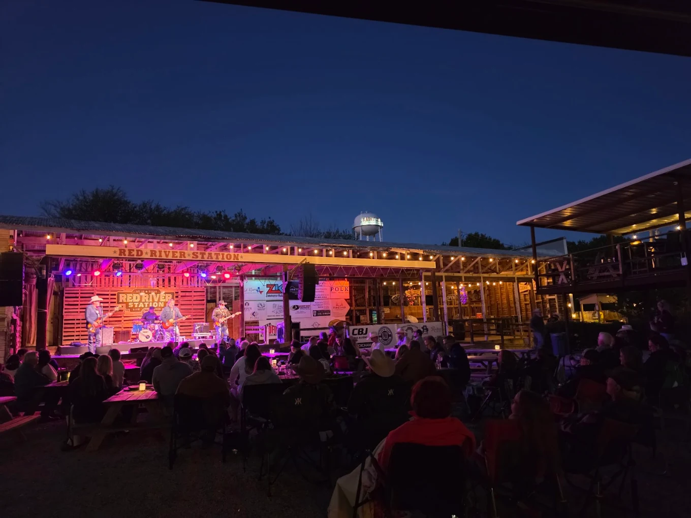 Blue-hour view of the stage and picnic tables with the Saint Jo water tower behind